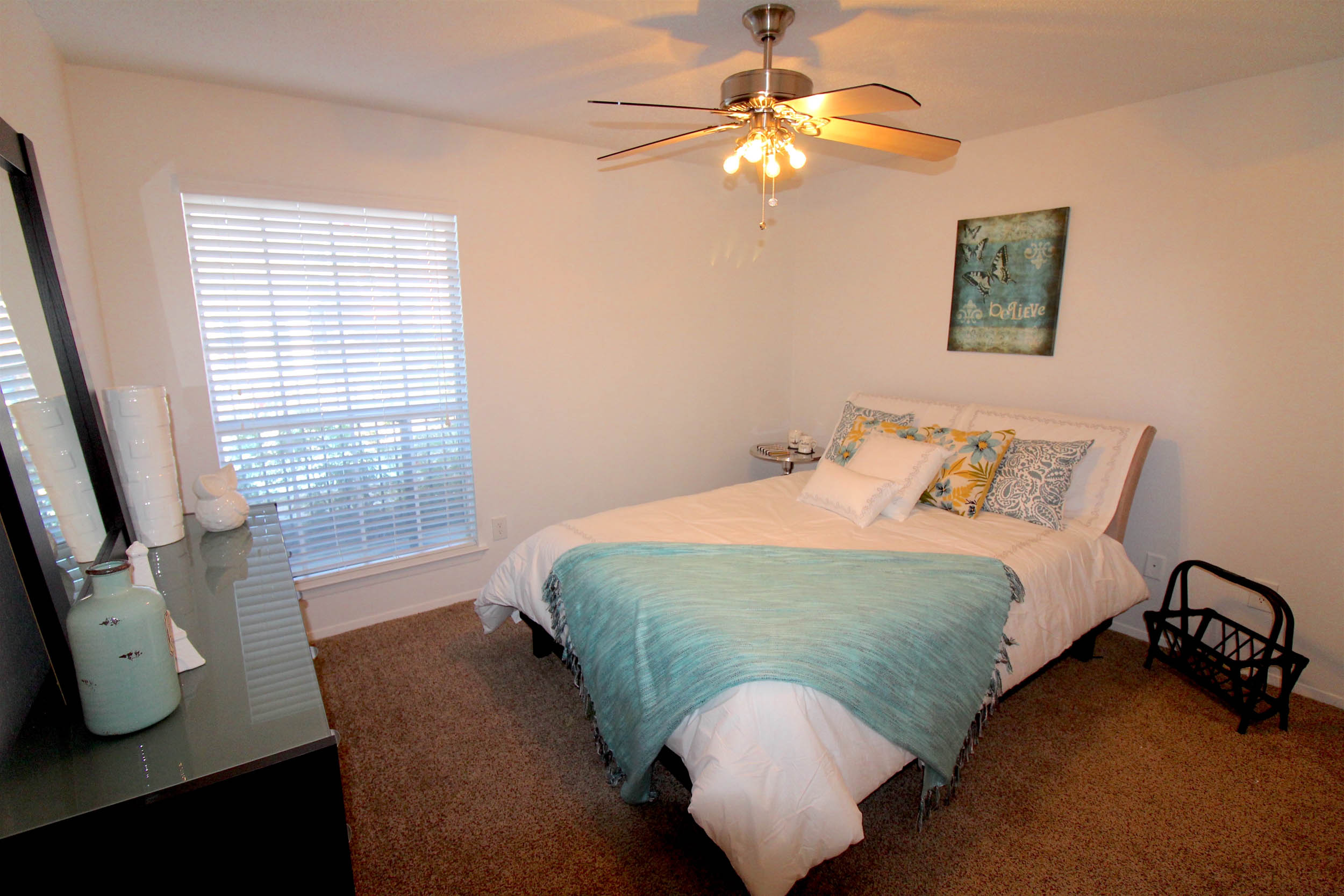 Bedroom with ceiling fan dresser and bed with teal decor